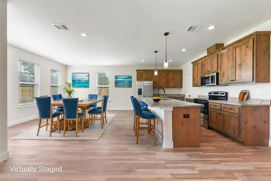 Virtually Staged Kitchen featuring stainless steel appliances, visible vents, light wood-type flooring, a kitchen bar, and brown cabinetry