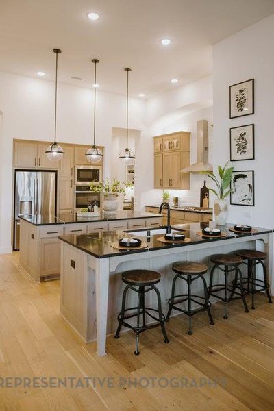 Kitchen featuring wall chimney exhaust hood, light brown cabinetry, a peninsula, dark countertops, and a breakfast bar area Kitchen featuring wall chimney exhaust hood, light brown cabinetry, a peninsula, dark countertops, and a breakfast bar area