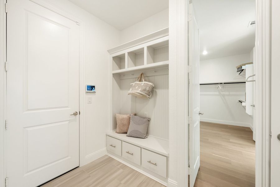Mudroom with built-in white cubbies, bench seat, drawers, and view into walk-in closet with light wood floors