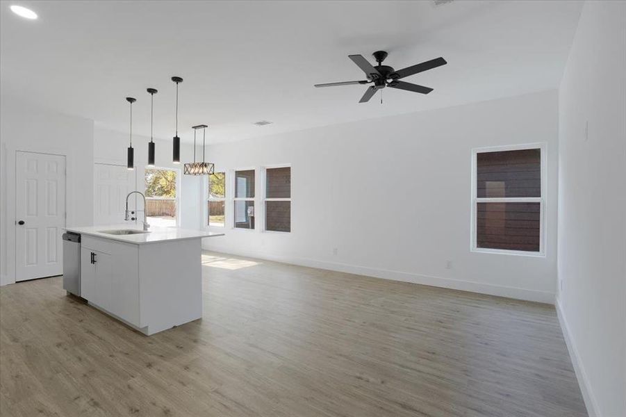 Kitchen featuring sink, pendant lighting, light hardwood / wood-style floors, a kitchen island with sink, and white cabinets