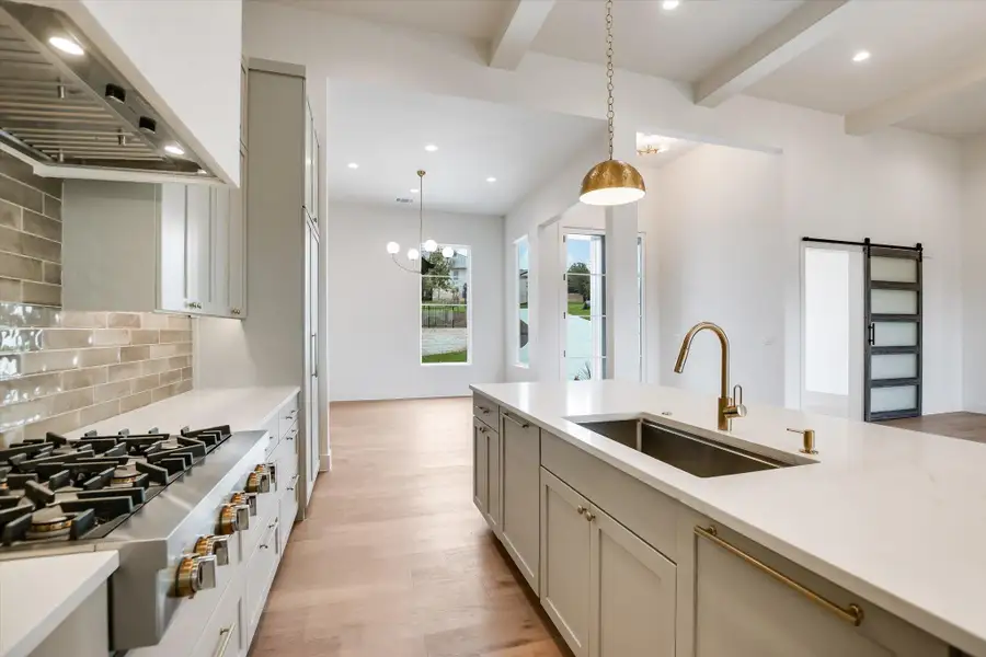 Modern kitchen featuring a large island with an undermount sink and brass faucet, stainless steel range with a brick-style backsplash, light cabinetry, and wood-finish flooring