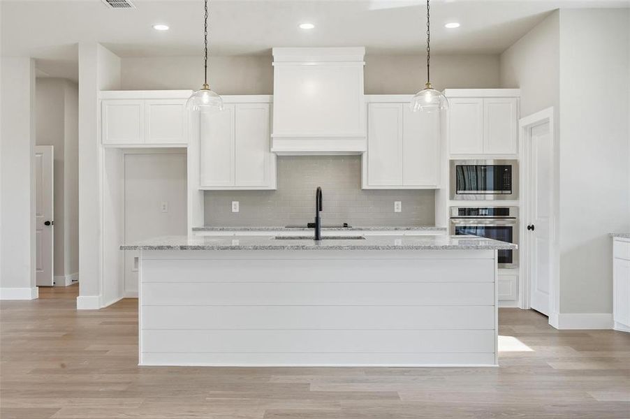 Kitchen with light stone countertops, stainless steel appliances, white cabinetry, and light wood finished floors
