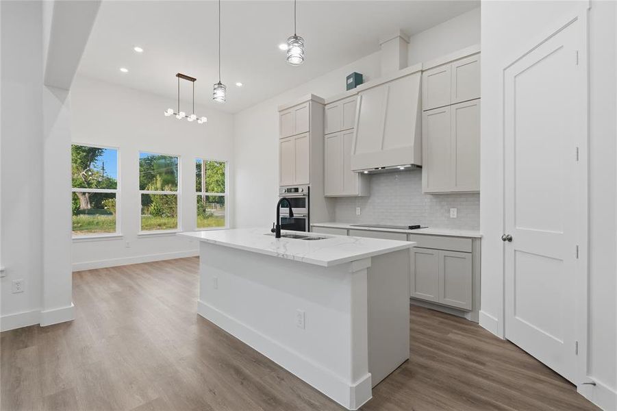 Modern kitchen featuring an island with a white countertop, light gray cabinetry, built-in appliances, and a white subway tile backsplash