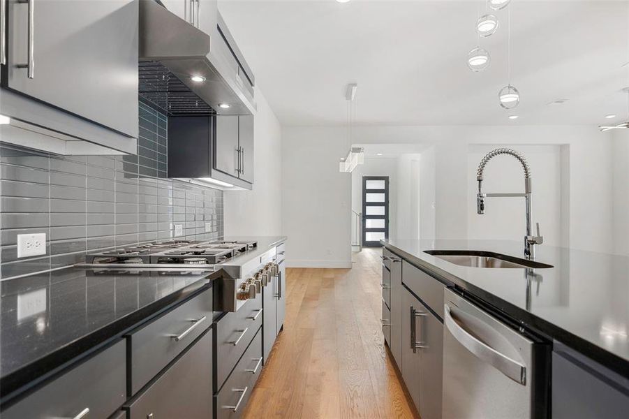 Kitchen with under cabinet range hood, stainless steel appliances, a sink, light wood-type flooring, and decorative backsplash