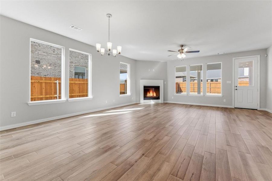 Unfurnished living room featuring a glass covered fireplace, hanging lights, ceiling fan, and light wood finished floors