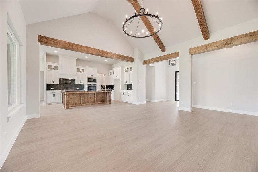 Unfurnished living room with a chandelier, light wood-type flooring, high vaulted ceiling, recessed lighting, and beam ceiling