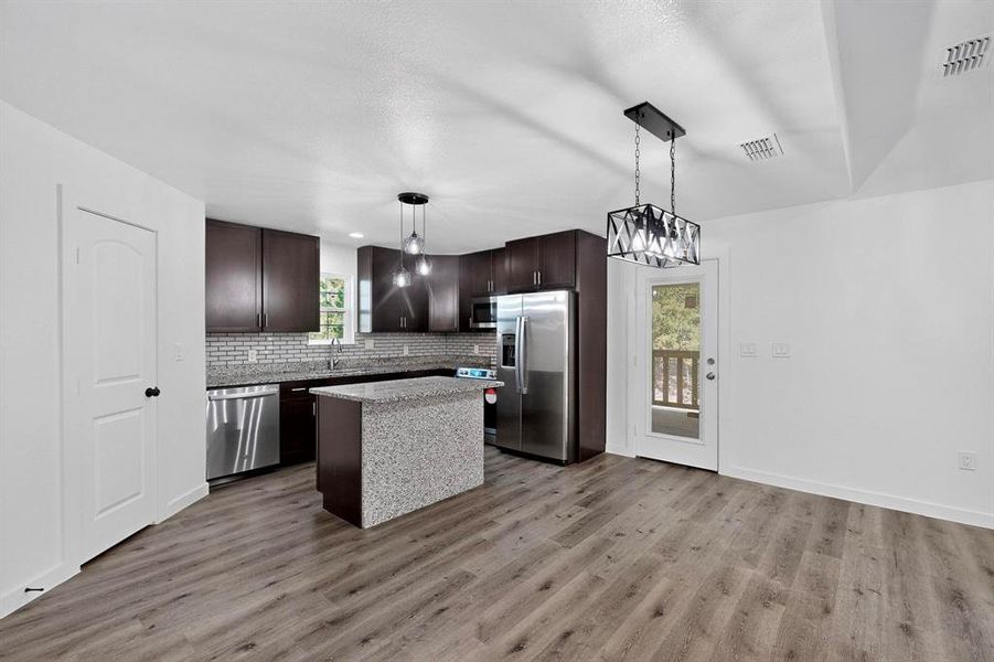 Kitchen with dark brown cabinets, pendant lighting, tasteful backsplash, a center island, and stainless steel appliances