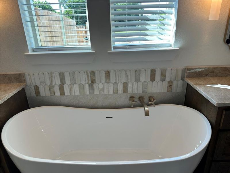Freestanding soaking tub with brushed nickel wall-mounted faucet, complemented by a decorative tile backsplash featuring an elongated picket pattern