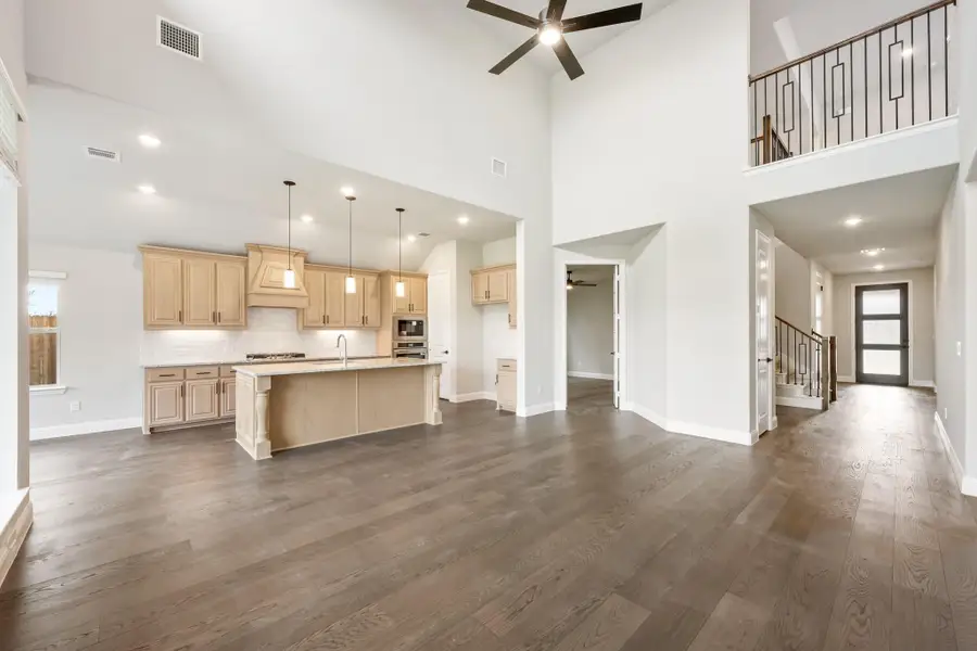 Open-concept living area with kitchen island, high ceilings, hardwood floors, and staircase visible in background. Open-concept living area with kitchen island, high ceilings, hardwood floors, and staircase visible in background.