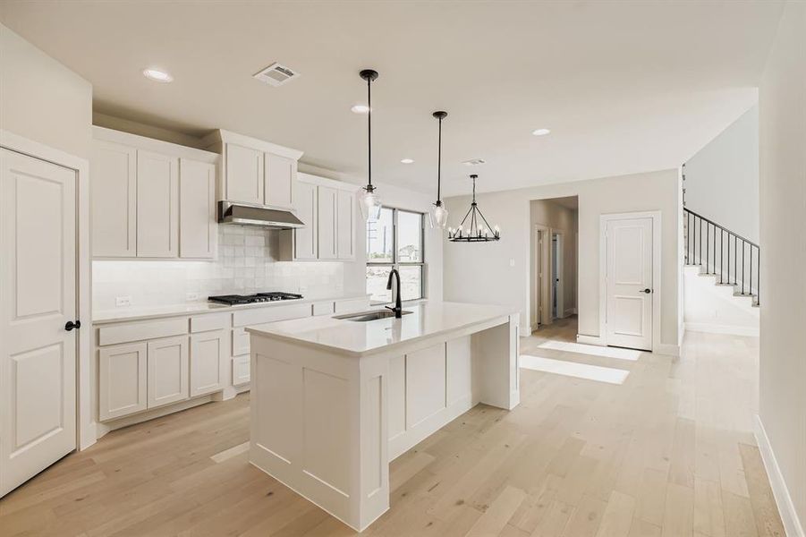Kitchen with light wood-type flooring, an island with sink, tasteful backsplash, light countertops, and recessed lighting
