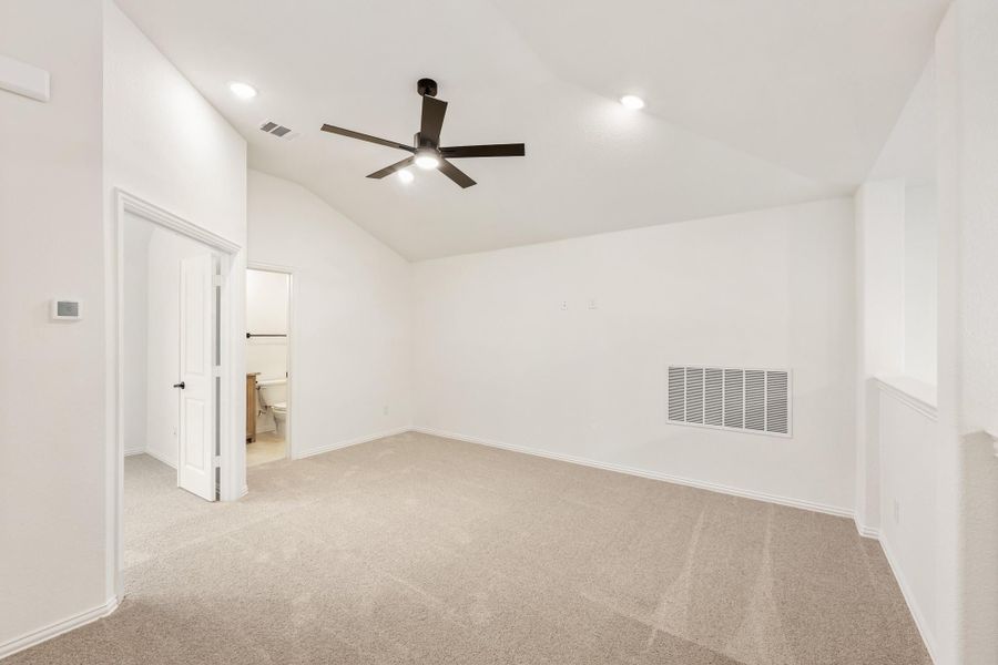 Empty bedroom with vaulted ceiling, ceiling fan, carpet flooring, and attached bathroom doorway Empty bedroom with vaulted ceiling, ceiling fan, carpet flooring, and attached bathroom doorway