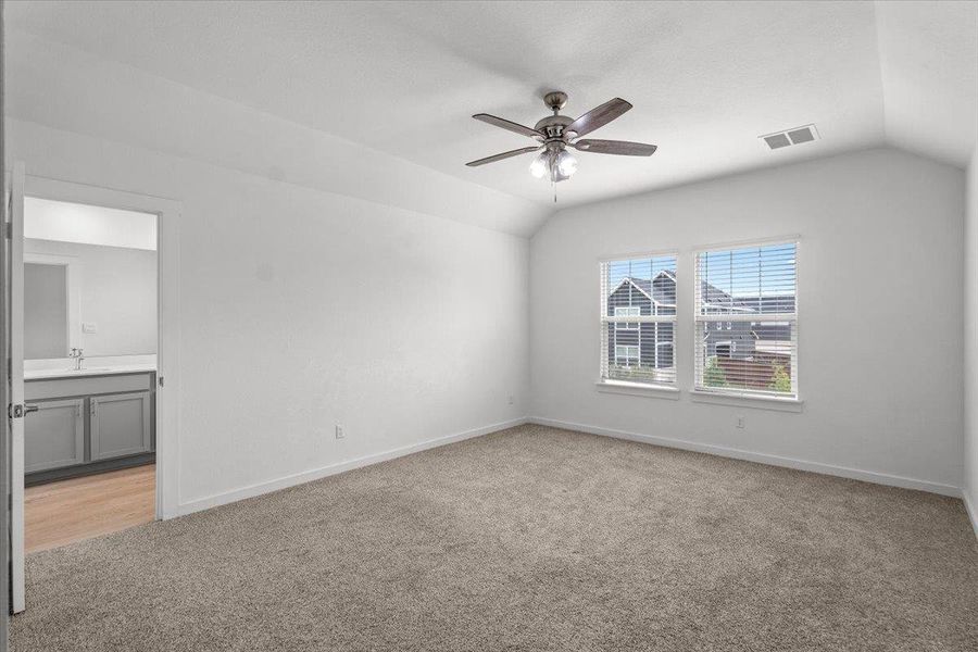 A spacious bedroom featuring neutral carpeting, a vaulted ceiling, and ample natural light from two windows.