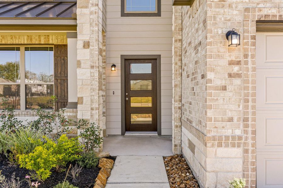The inviting covered front porch enhances the home's striking curb appeal. This welcoming entry features robust white columns and a modern, dark wood front door with vertical glass panels, set against a backdrop of light-toned mixed masonry and siding. The inviting covered front porch enhances the home's striking curb appeal. This welcoming entry features robust white columns and a modern, dark wood front door with vertical glass panels, set against a backdrop of light-toned mixed masonry and siding.