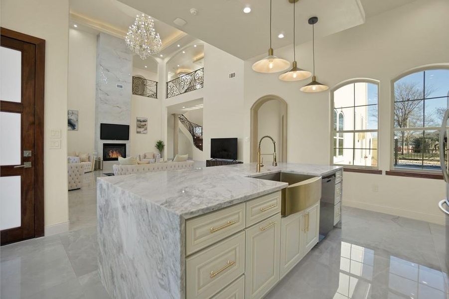 Kitchen featuring black dishwasher, hanging light fixtures, a kitchen island with sink, light stone counters, and a premium fireplace