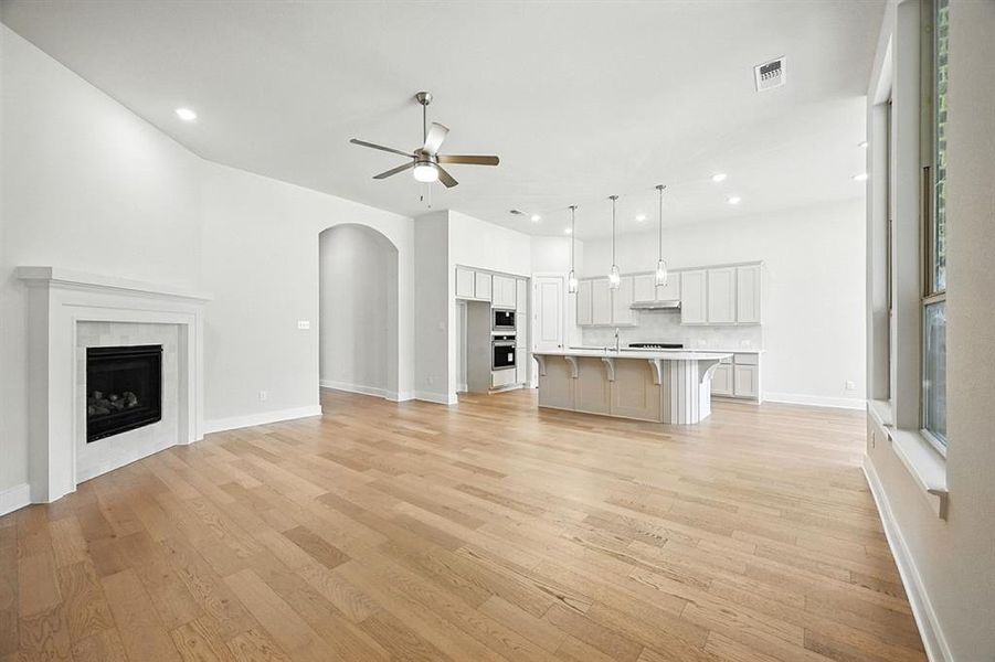 Unfurnished living room featuring a tile fireplace, arched walkways, light wood-style floors, recessed lighting, and a ceiling fan Unfurnished living room featuring a tile fireplace, arched walkways, light wood-style floors, recessed lighting, and a ceiling fan