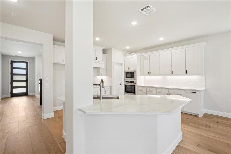 Kitchen with appliances with stainless steel finishes, a sink, light wood-type flooring, white cabinetry, and baseboards