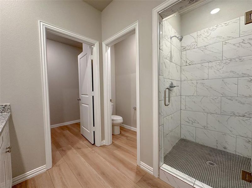 Bathroom with toilet, a shower with door, wood-type flooring, and vanity