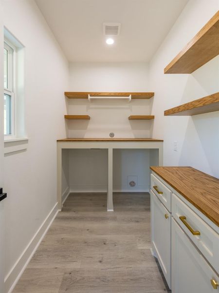 This room features a bright, well-lit space with light wood flooring and white walls. It includes built-in wooden shelves and a countertop, ideal for storage or workspace. The cabinetry provides additional storage, and a window brings in natural light.
