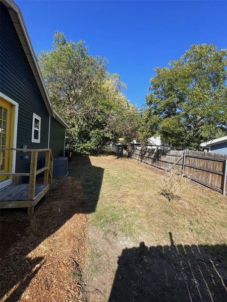Expansive backyard featuring a wood privacy fence, mature trees, and a wooden deck with railing
