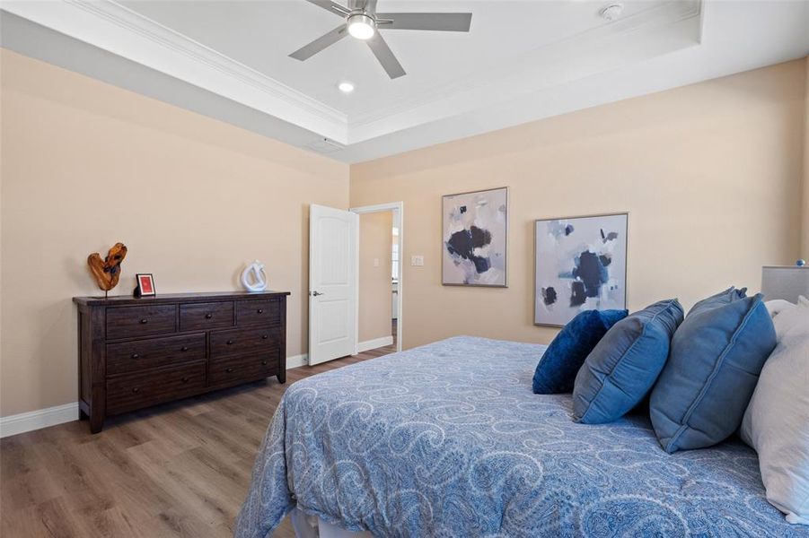 Bedroom featuring wood-finish flooring, neutral wall tones, and a tray ceiling with crown molding Bedroom featuring wood-finish flooring, neutral wall tones, and a tray ceiling with crown molding
