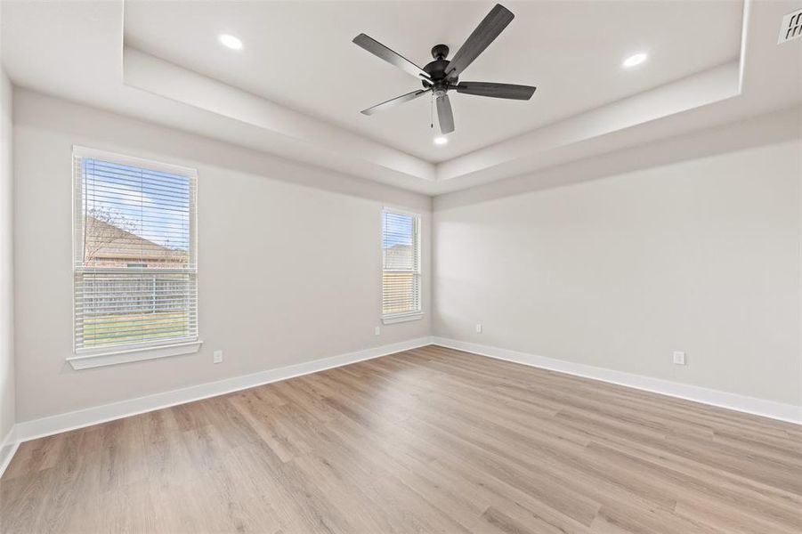 Unfurnished room with light wood finished floors, recessed lighting, a ceiling fan, plenty of natural light, and a tray ceiling