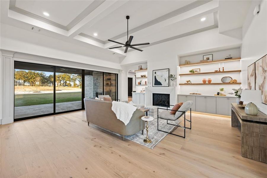 Living area featuring built in features, a fireplace, ceiling fan, light wood finished floors, and beamed ceiling Living area featuring built in features, a fireplace, ceiling fan, light wood finished floors, and beamed ceiling