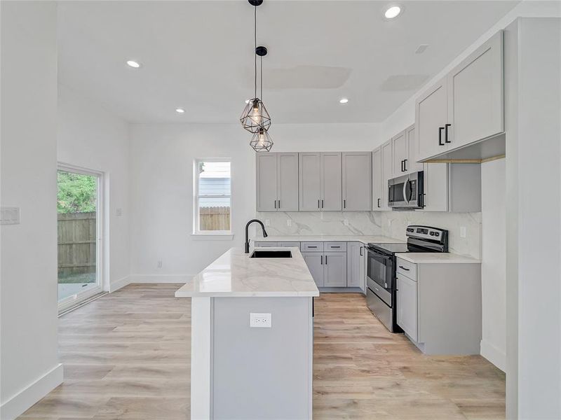 Kitchen featuring appliances with stainless steel finishes, light hardwood / wood-style floors, tasteful backsplash, sink, and a kitchen island with sink