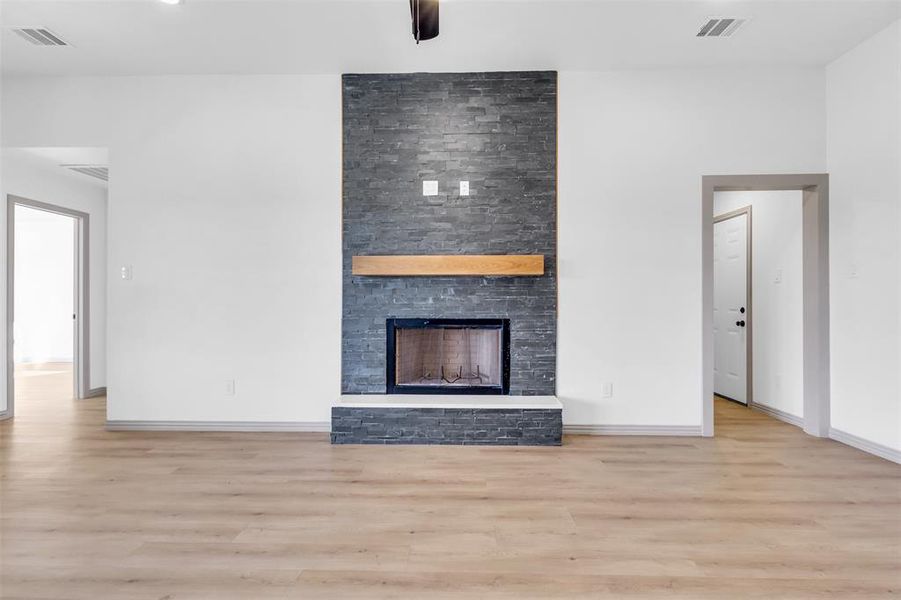 Unfurnished living room with light hardwood / wood-style floors, a stone fireplace, and ceiling fan