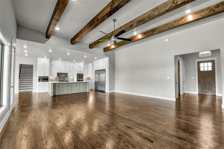 Unfurnished living room with beam ceiling, dark wood-type flooring, and ceiling fan