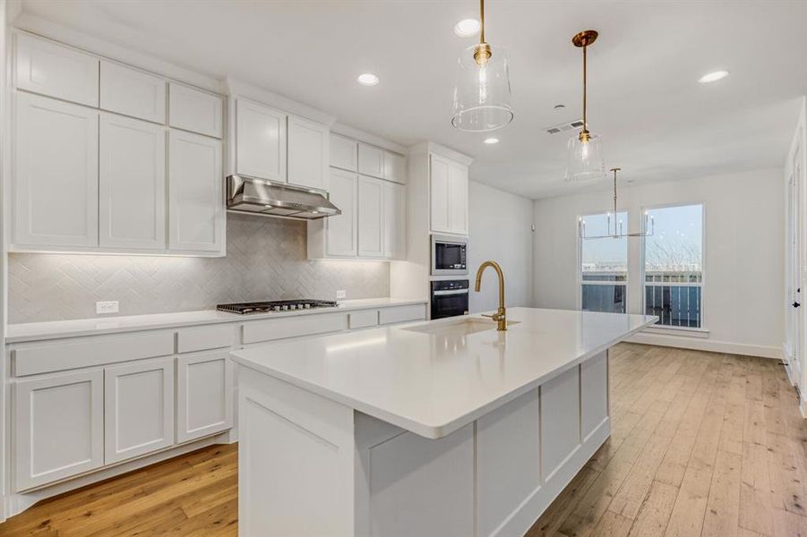 Kitchen with white cabinets, decorative backsplash, a center island with sink, light wood-type flooring, and decorative light fixtures