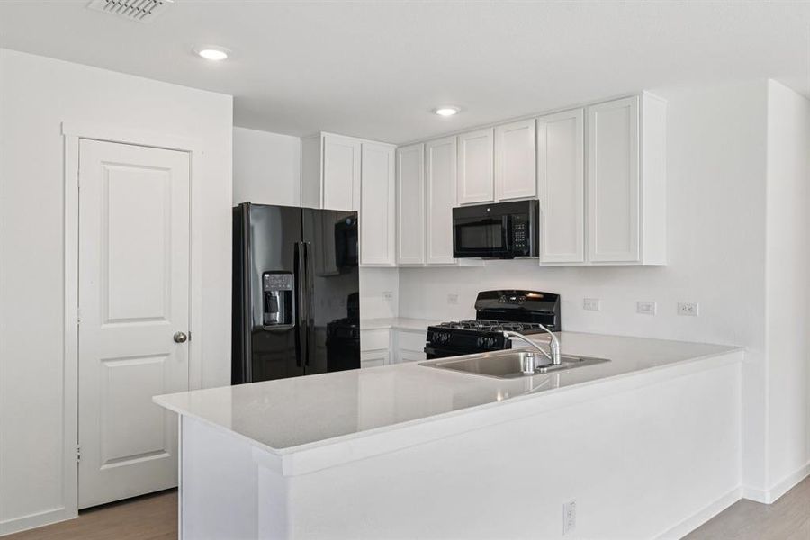 Kitchen featuring black appliances, a peninsula, light wood-style flooring, light countertops, and white cabinets Kitchen featuring black appliances, a peninsula, light wood-style flooring, light countertops, and white cabinets