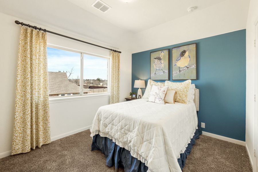 Bedroom with blue accent wall, carpet flooring, large window, and queen bed with white bedding