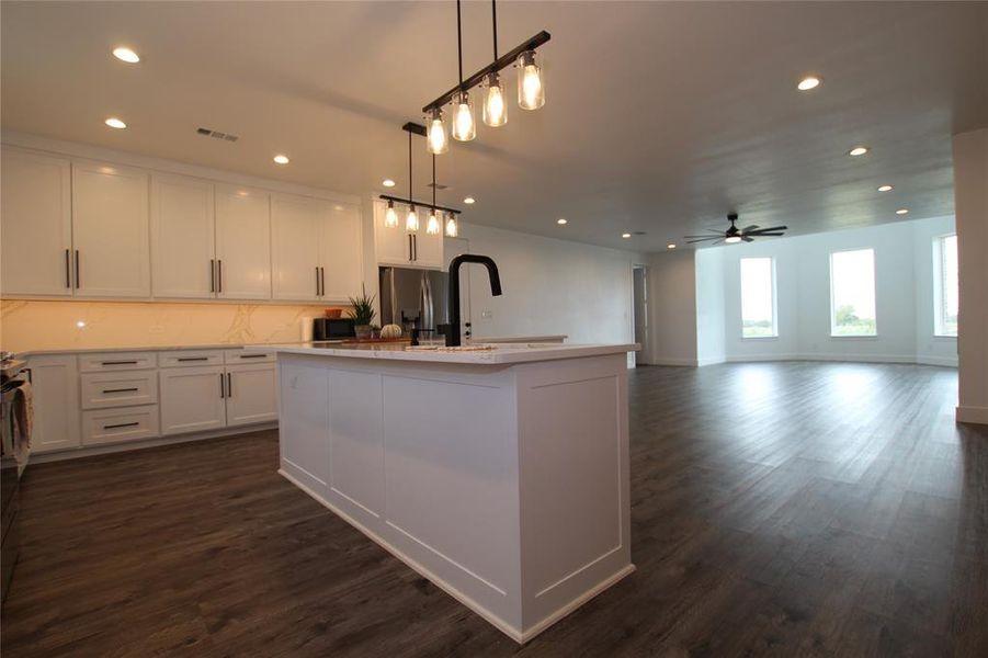 Kitchen with a center island with sink, pendant lighting, white cabinetry, recessed lighting, and dark wood-style floors Kitchen with a center island with sink, pendant lighting, white cabinetry, recessed lighting, and dark wood-style floors