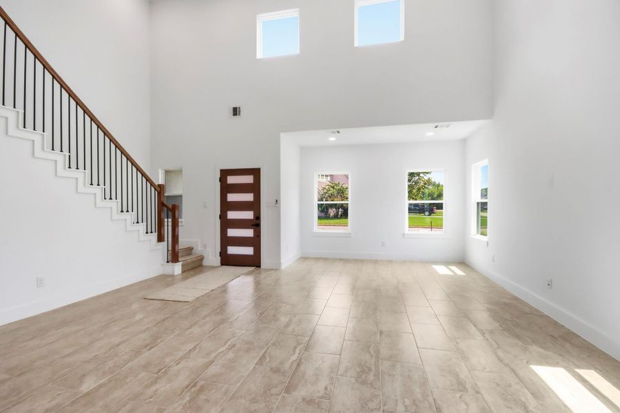 Bright and spacious living area with high ceilings, large windows, and sleek flooring, complemented by a modern staircase and contemporary front door.