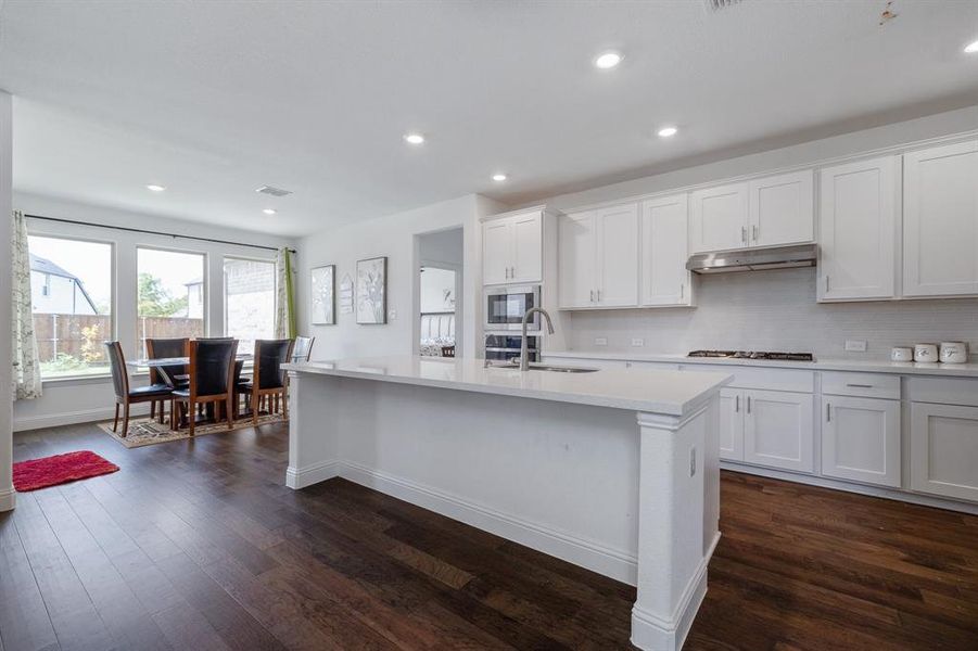 Kitchen with dark wood finished floors, built in microwave, light countertops, under cabinet range hood, and a sink