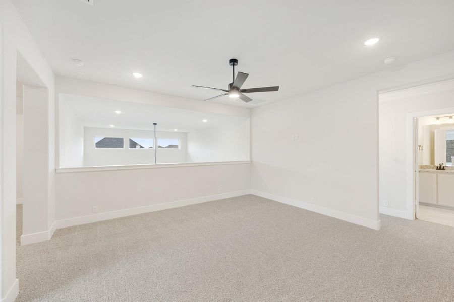 Empty bedroom with beige carpet, ceiling fan, and ensuite bathroom doorway visible