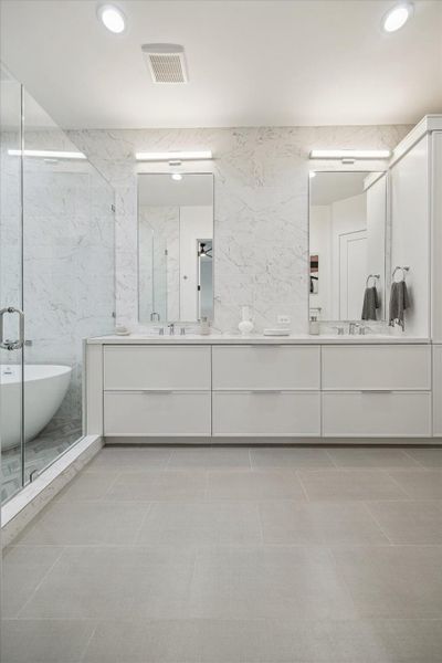 Expansive dual-sink vanity framed by full-height marble-look walls and modern linear lighting. Wide-format flooring grounds the space while oversized mirrors amplify light and dimension. Crisp cabinetry lines and seamless surfaces create a refined, contemporary aesthetic, offering generous storage and a polished, spa-like environment within the private primary suite.