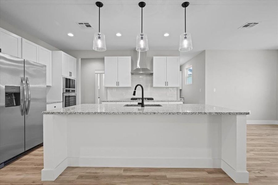 Kitchen with stainless steel fridge, wall chimney range hood, recessed lighting, white cabinets, and a large island