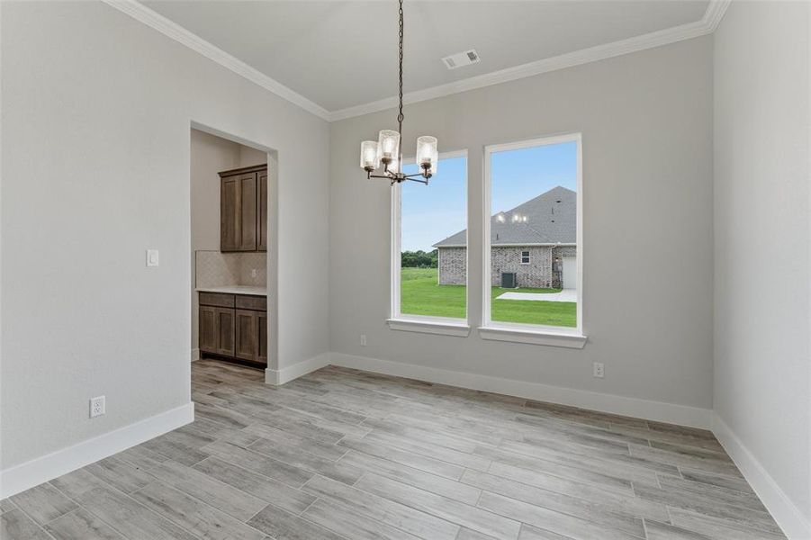 Spacious room featuring wood-finish tile flooring, a contemporary chandelier, two large windows, white baseboards, and crown molding