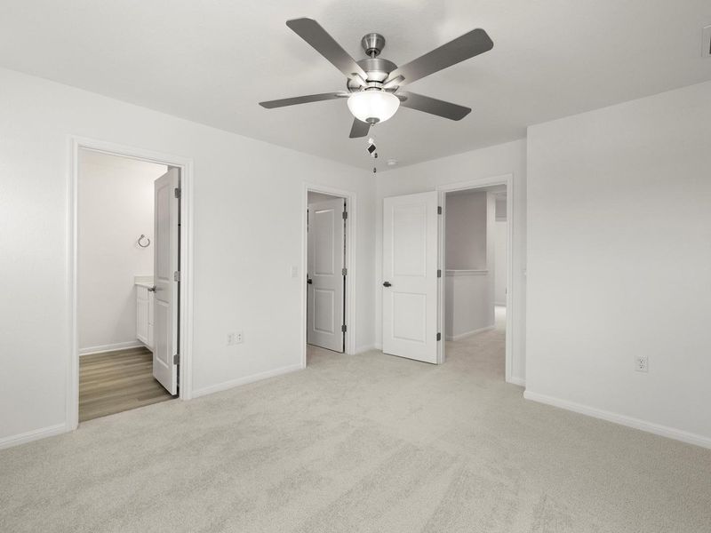 A well-lit bedroom provides ample space and neutral carpeting, featuring a ceiling fan for comfort.
