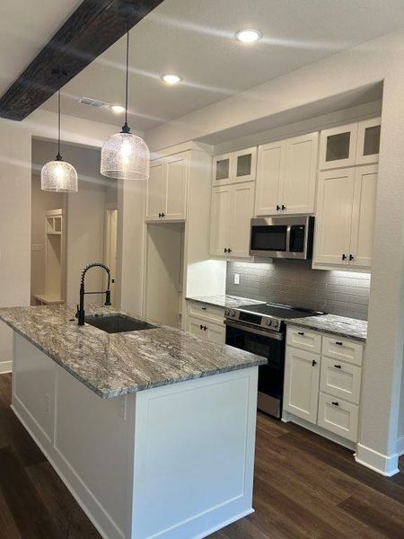 Kitchen featuring stainless steel appliances, white cabinetry, decorative light fixtures, and sink