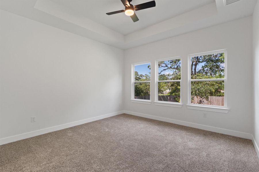 Spacious room featuring three large windows, tray ceiling, and a ceiling fan