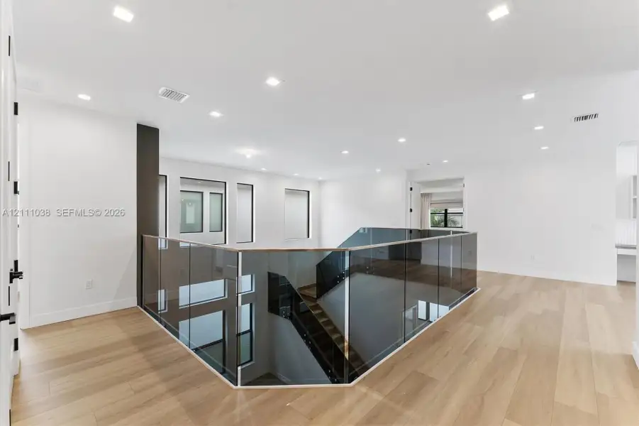Open landing featuring wood-finish flooring, recessed lighting, and a frameless glass railing system