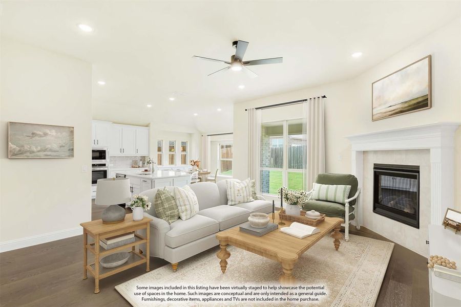 Open living room with fireplace, ceiling fan, and view into white kitchen with large windows Open living room with fireplace, ceiling fan, and view into white kitchen with large windows