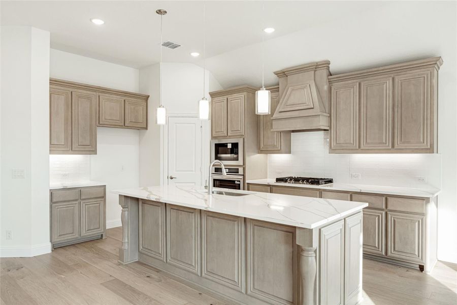 Kitchen with gray-brown cabinets, large marble island, stainless steel appliances, and pendant lights over hardwood floors