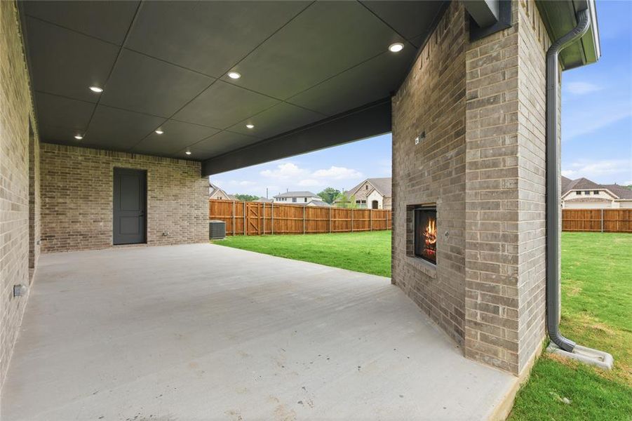 Expansive covered patio featuring a brick exterior with an outdoor fireplace, recessed lighting, and a grey plank ceiling Expansive covered patio featuring a brick exterior with an outdoor fireplace, recessed lighting, and a grey plank ceiling