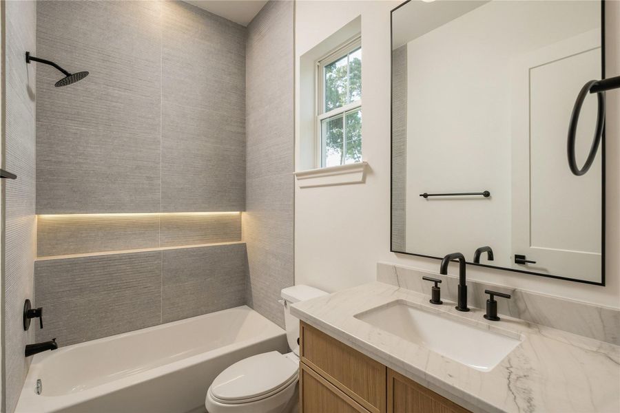 A well-appointed secondary bath features a frameless glass shower, full-height designer tile, and an illuminated shower niche, continuing the home’s attention to detail across every ensuite.