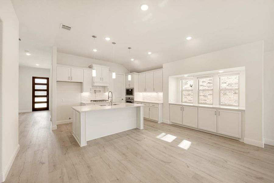 Open kitchen with white cabinets, center island, pendant lights, and light wood floors