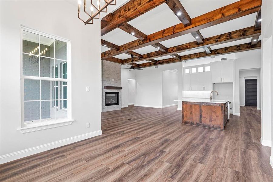 Kitchen with a stone fireplace, ceiling fan with notable chandelier, a kitchen island with sink, and dark wood-type flooring