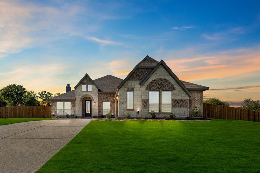 Single-story home with brick and stone exterior, arched entry, dark roof, and large front lawn with concrete driveway